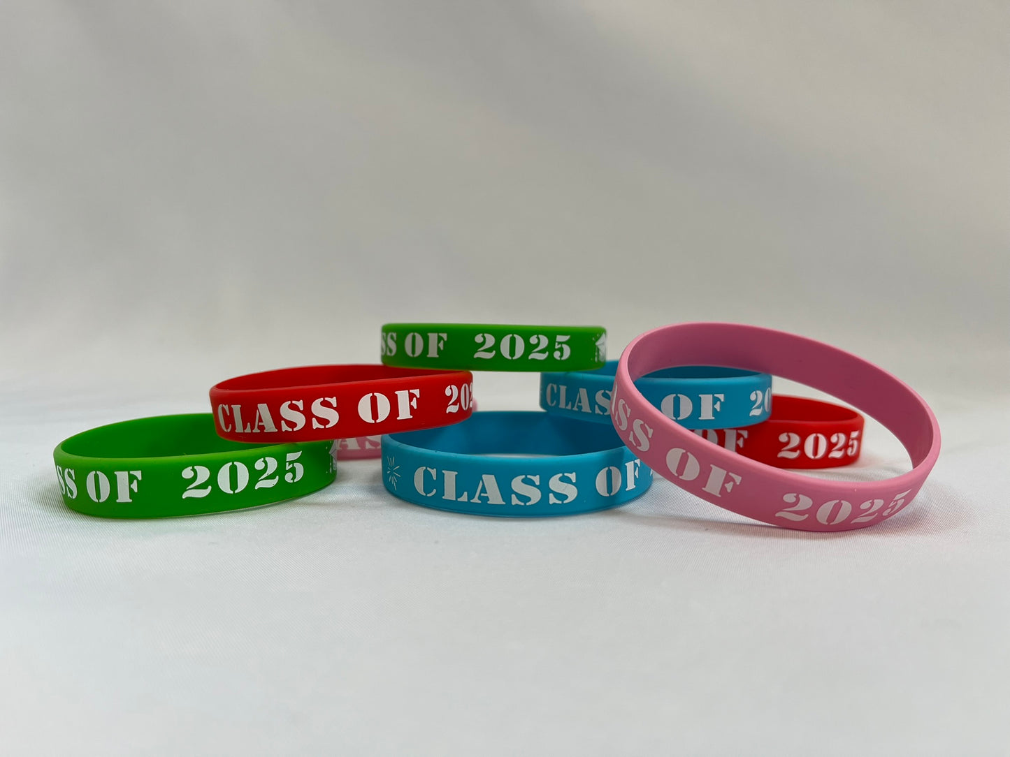 A pile of rubber wristbands in green, red, blue and pink. Each has white writing on that says “class of 2025”.