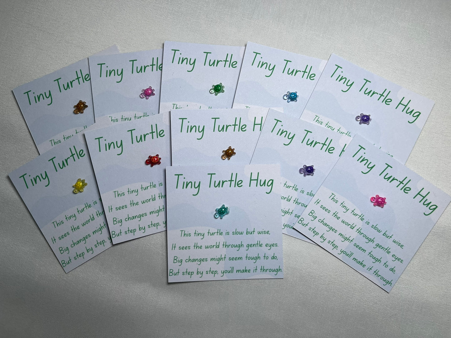 A small plastic turtle is stuck to a piece of card, with waves in the background. The card is titled “tiny turtle hug” and has a poem underneath about big changes. There are a number of cards, all with different colour turtles – gold, pink, green, blue, purple, yellow, red.