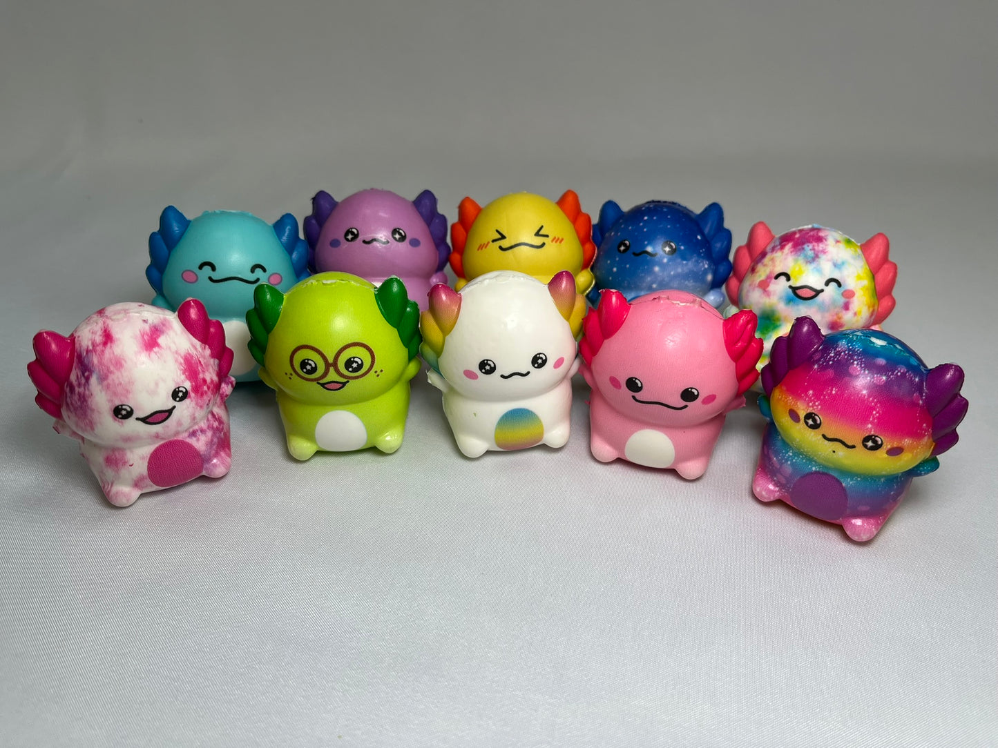 Two rows of squishy axolotl toys. They are all different colours with different facial expressions. They look fun and whimsical.