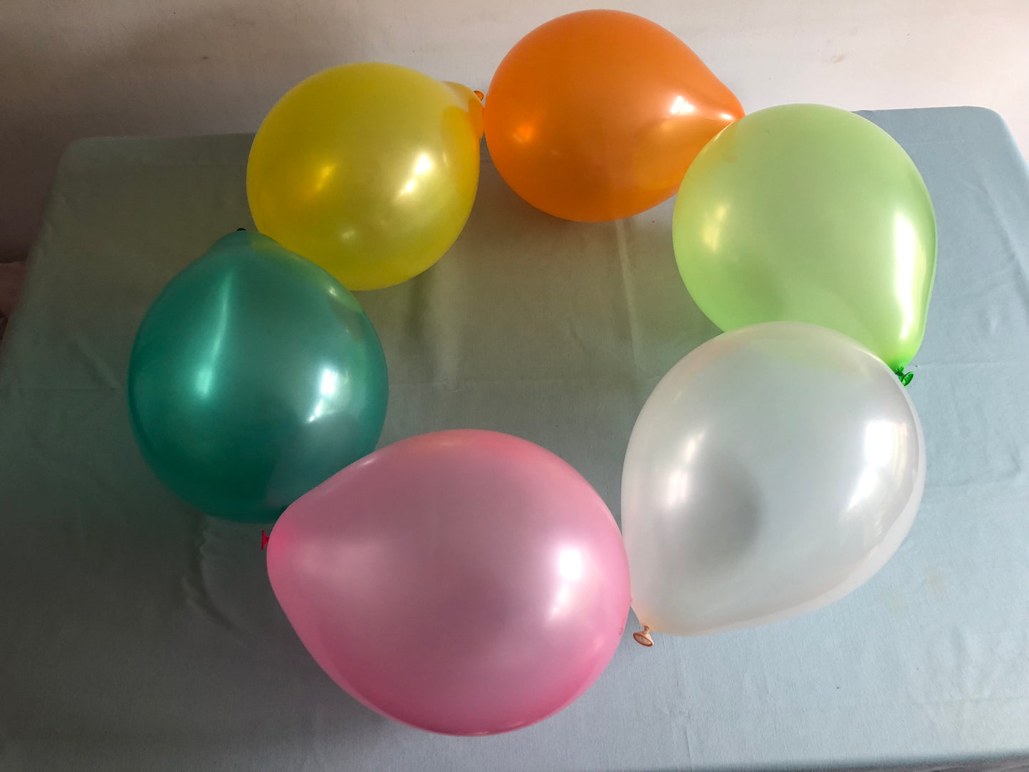 Six blown up balloons a glued together in a ring. They are green, yellow, orange, white and pink.