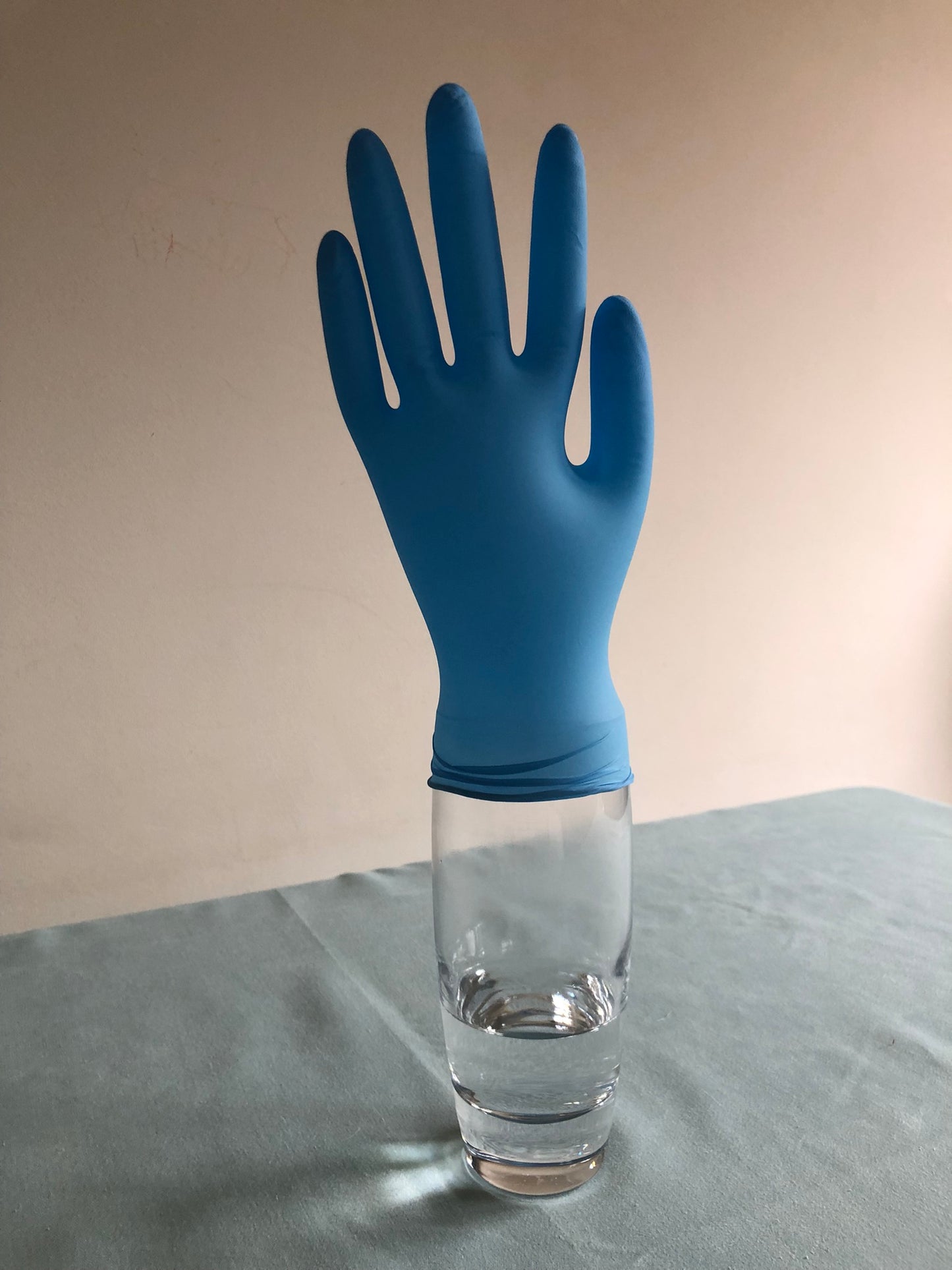 An inflated blue glove is on top of a glass with some clear liquid in.
