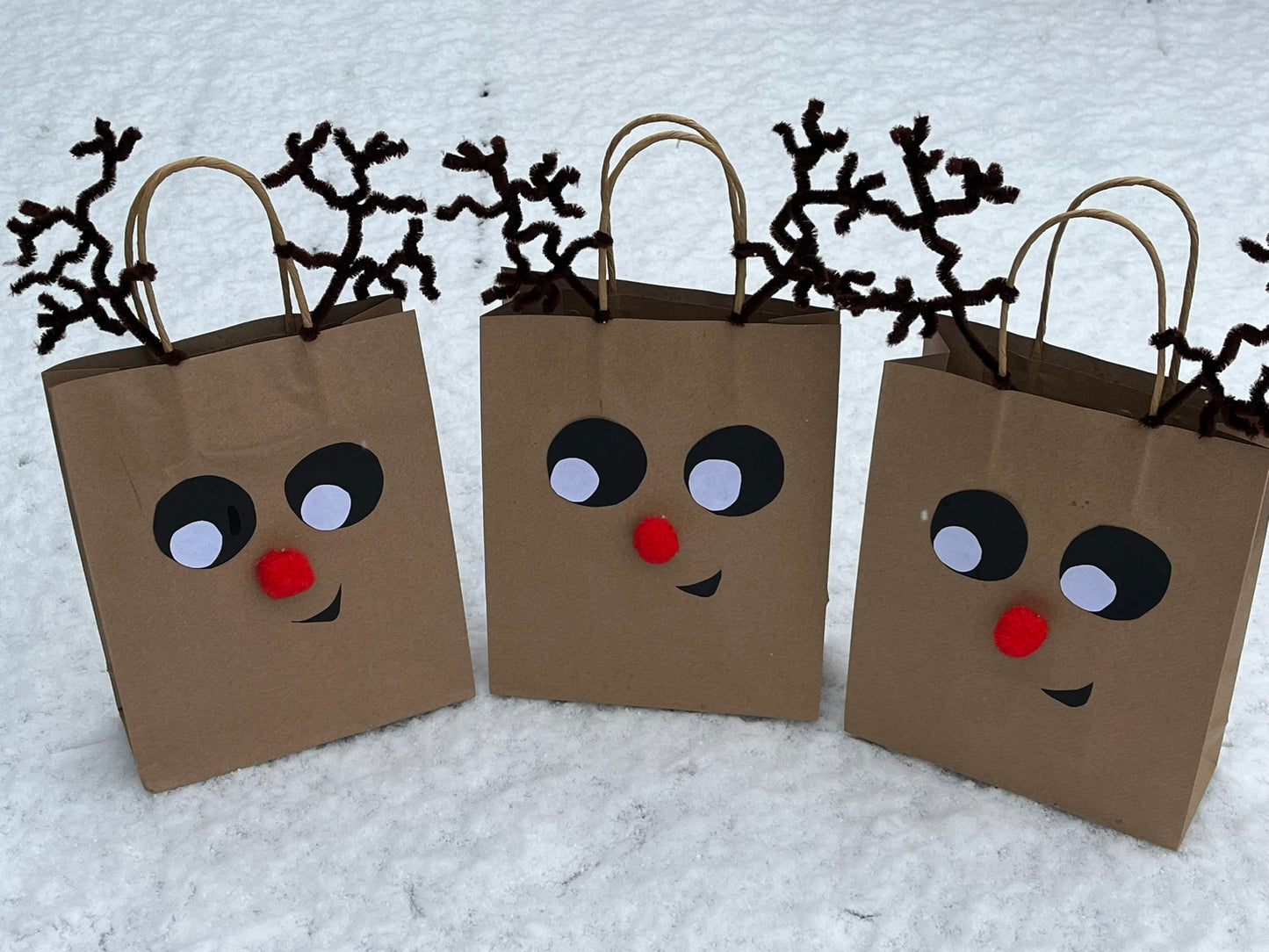 Three brown paper party bags are decorated to look like reindeer faces.