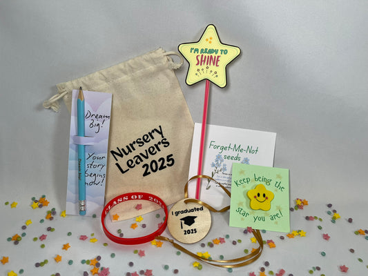 A white canvas bag reading "Nursery Leavers 2025" sits on a confetti background. The contents are shown: a blue pencil printed with "dream big", a red wristband that says Class of 2025, a yellow star rubber with a smile sits on a card titled “keep being the star you are”, a wooden circular medal has a graduation hat on it and the words “I graduated 2025”, there is a packet of Forget-Me-Not seeds. There’s a red glowstick with a star at the top, it looks like a magic wand, and reads Ready to Shine