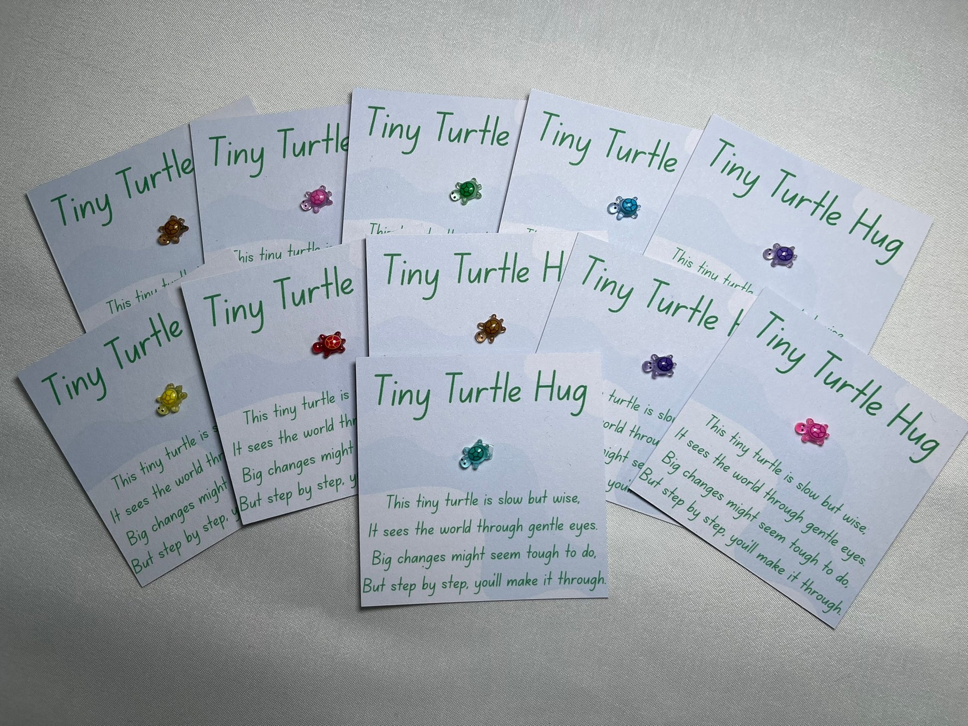A small plastic turtle is stuck to a piece of card, with waves in the background. The card is titled “tiny turtle hug” and has a poem underneath about big changes. There are a number of cards, all with different colour turtles – gold, pink, green, blue, purple, yellow, red.