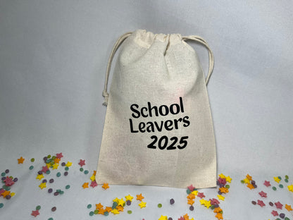 A white canvas bag is on a bed of confetti and sprinkles. The bag is drawstring, and printed with the words “school leavers 2025”.