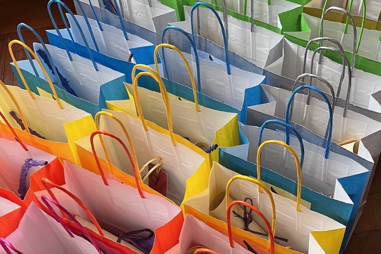 The image looks at 3 rows of filled party bags from above. We can see scrolls, wands and bookmarks poking out of the top. The bags are brightly coloured - pink, orange, yellow, blue, silver, green, gold.