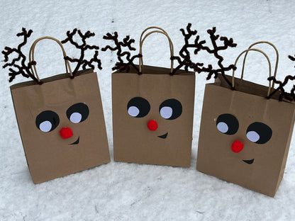 Three brown paper party bags are decorated to look like reindeer faces.