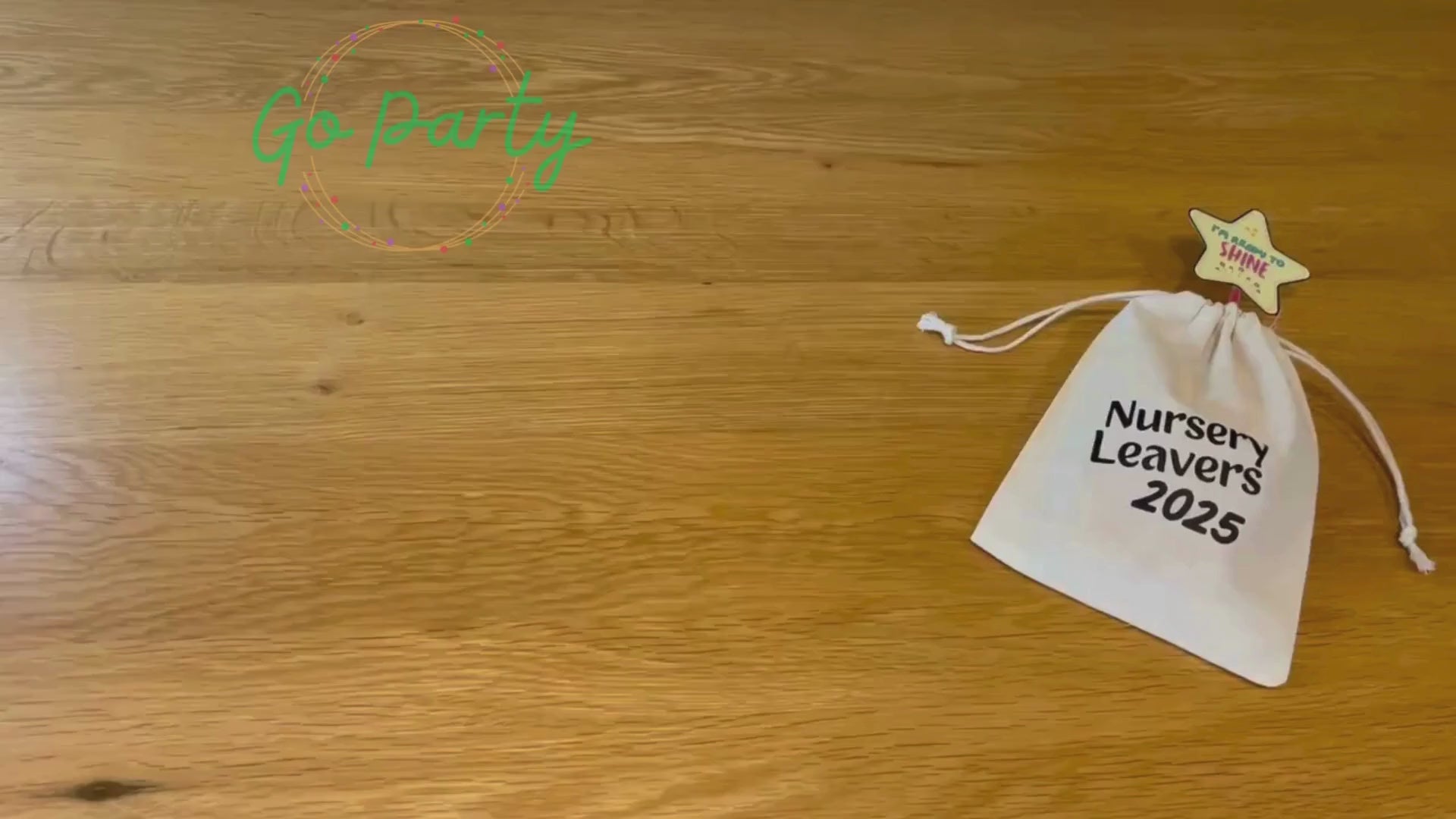 An unboxing video of the Nursery Leavers 2025 bag: there is a glowstick wands with a star on top, a blue pencil on a card saying dream big, a white envelope labelled forget-me-not seeds, a wooden circular medal that has a graduation cap and I graduated 2025 on it, a red class of 2025 wristband, and a yellow smiley star rubber on a card reading keep being the star you are. They are all laid out on a wooden surface. 