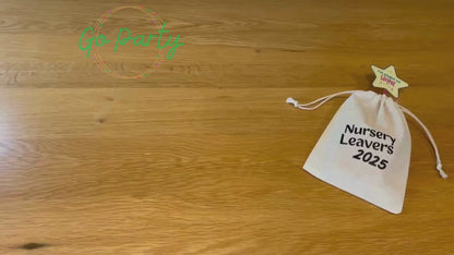 An unboxing video of the Nursery Leavers 2025 bag: there is a glowstick wands with a star on top, a blue pencil on a card saying dream big, a white envelope labelled forget-me-not seeds, a wooden circular medal that has a graduation cap and I graduated 2025 on it, a red class of 2025 wristband, and a yellow smiley star rubber on a card reading keep being the star you are. They are all laid out on a wooden surface. 