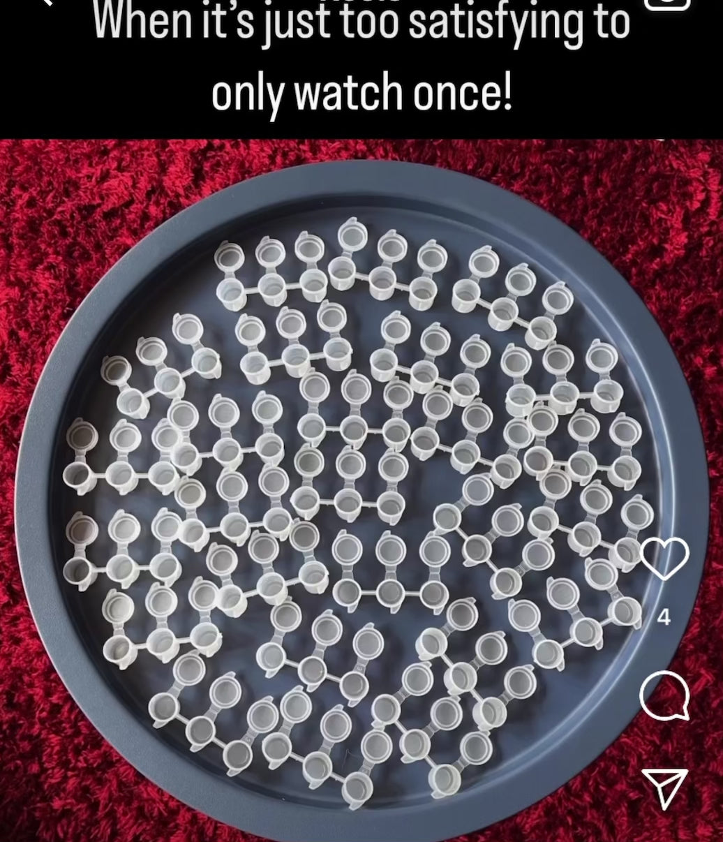 The video caption is "When it's just too satisfying to only watch once!". A blue table is full of empty pots. In stop-motion style, they are filled with blue, yellow, and then red paint. At the end all the lids snap shut.