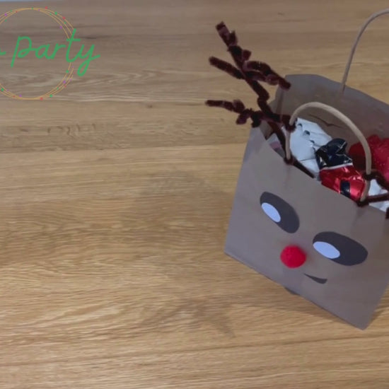 Video showing a Party Bag being unpacked. The party bag is decorated to look like a reindeer face.
First comes out a Santa balloon bracelet, then a gingerbread cutter and biscuit recipe, then four squishy snowballs, a red striped bag labelled “Candy Cane Craft”, then plantable wildflower seed paper shaped as a Christmas Tree, Reindeer food in an envelope is shaken, lastly a wreath colouring sheet and two rainbow was crayons shaped as snowflakes.