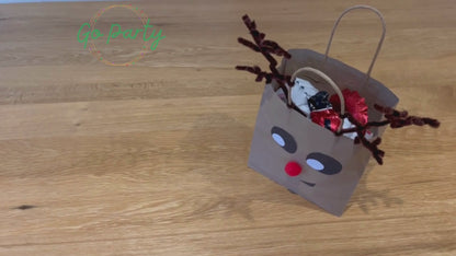 Video showing a Party Bag being unpacked. The party bag is decorated to look like a reindeer face.
First comes out a Santa balloon bracelet, then a gingerbread cutter and biscuit recipe, then four squishy snowballs, a red striped bag labelled “Candy Cane Craft”, then plantable wildflower seed paper shaped as a Christmas Tree, Reindeer food in an envelope is shaken, lastly a wreath colouring sheet and two rainbow was crayons shaped as snowflakes.