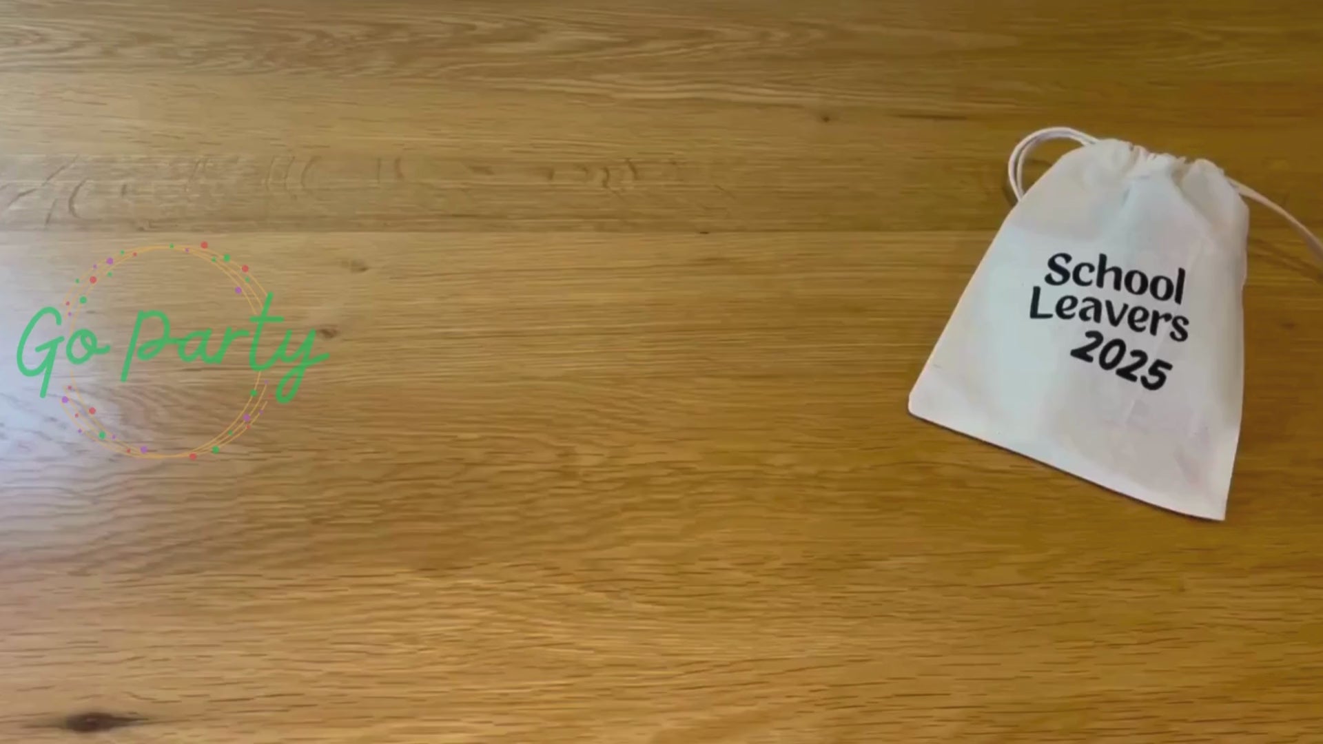 An unboxing video of the School Leavers 2025 bag: there is a blue class of 2025 wristband, a yellow pencil on a card saying dream big, a rainbow coloured axolotl squishy toy, a white envelope labelled forget-me-not seeds, a card with a turtle on titled tiny turtle hug, and a pink circular keyring that has a school leavers 2025 hoody on it. They are all laid out on a wooden surface.