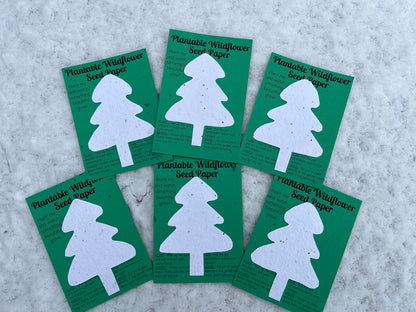 White paper cut into the shape of a Christmas Tree, stuck onto green card, labelled "Plantable Wildflower Seed Paper". There are six sheets sitting on snow, and each sheet has sowing instructions.